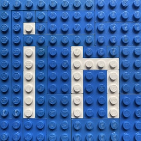 A flat arrangement of blue and white LEGO bricks, forming the word 'IN'. The background is predominantly blue, with the letters created using white bricks.