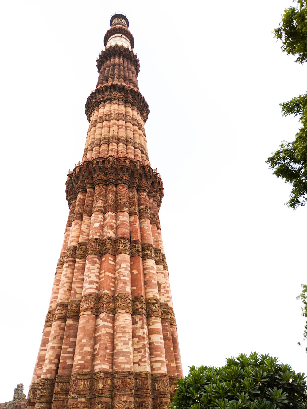 a tall tower with trees around it with Qutub Minar in the background