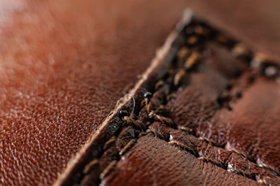 Close-up of rich brown leather pieces stitched by hand on a wooden workbench