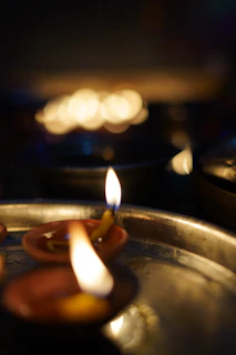 Softly lit camphor flames flickering gently on a decorated silver plate during a puja.