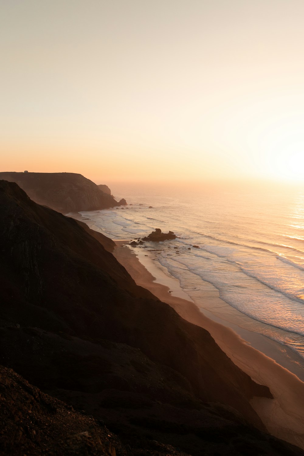 uma praia com um corpo de água e um grande penhasco rochoso