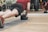 A person is performing a plank exercise on a mat, using a medicine ball for added balance and difficulty. The individual is dressed in athletic wear, including a red shirt and black shorts. This activity is taking place in a gym setting, as indicated by the mirrored wall and various exercise equipment in the background.