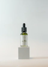 Close-up of Herbavita hair oil bottle surrounded by fresh herbal leaves and nuts.