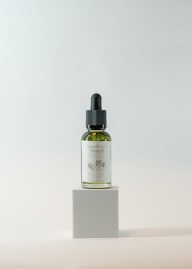 Close-up of a glass bottle filled with golden hair oil surrounded by fresh herbs and flowers on a wooden table.