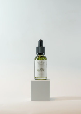 Close-up of a bottle of hair oil with fresh botanical ingredients around it.