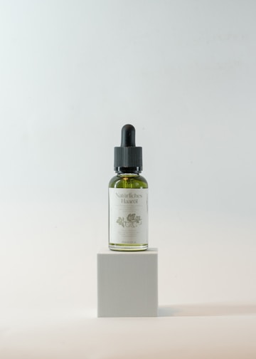 A close-up of a glass bottle filled with golden organic hair oil surrounded by fresh herbs and flowers.