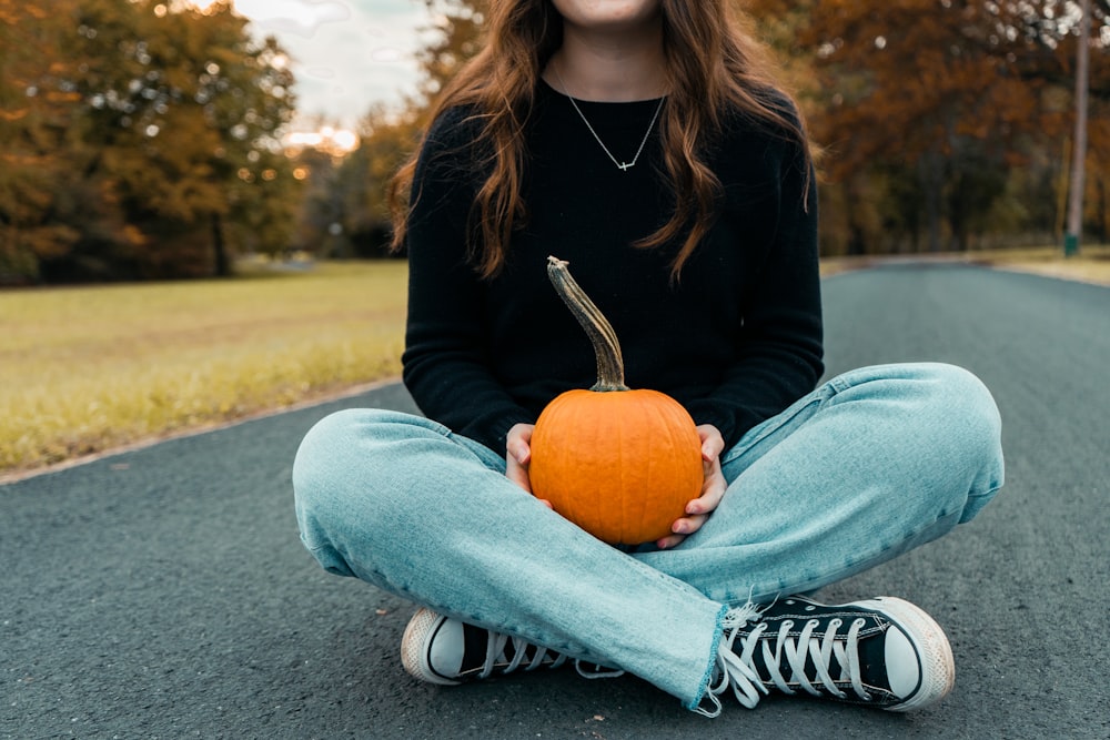 a woman sitting on the ground holding a pumpkin
