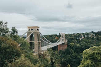 a stone bridge over a forest with Clifton Suspension Bridge in the background