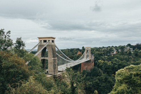a stone bridge over a forest with Clifton Suspension Bridge in the background