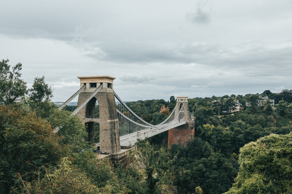 a stone bridge over a forest with Clifton Suspension Bridge in the background