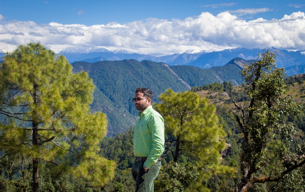 a man standing on a hill with trees and mountains in the background