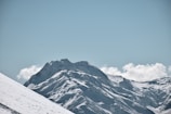 Snow-covered mountain peaks under a clear blue sky, with a lone hiker in the distance.