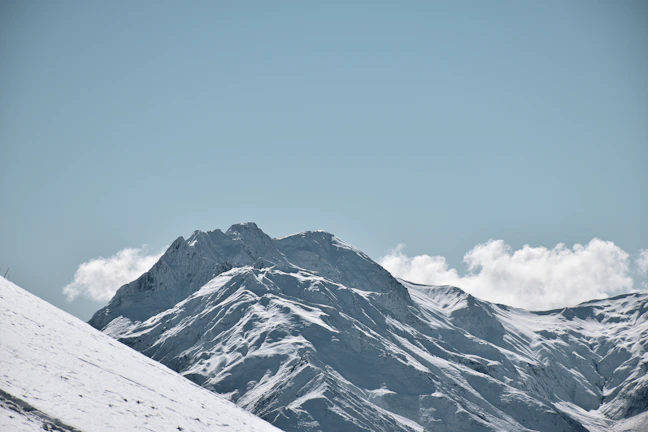 Snow-covered mountain peaks under a clear blue sky with a lone hiker in the distance.