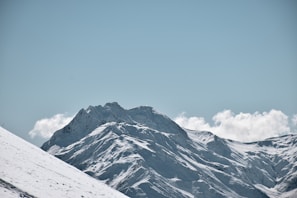 Snow-covered mountain peaks under a clear blue sky, with a lone hiker in the distance.