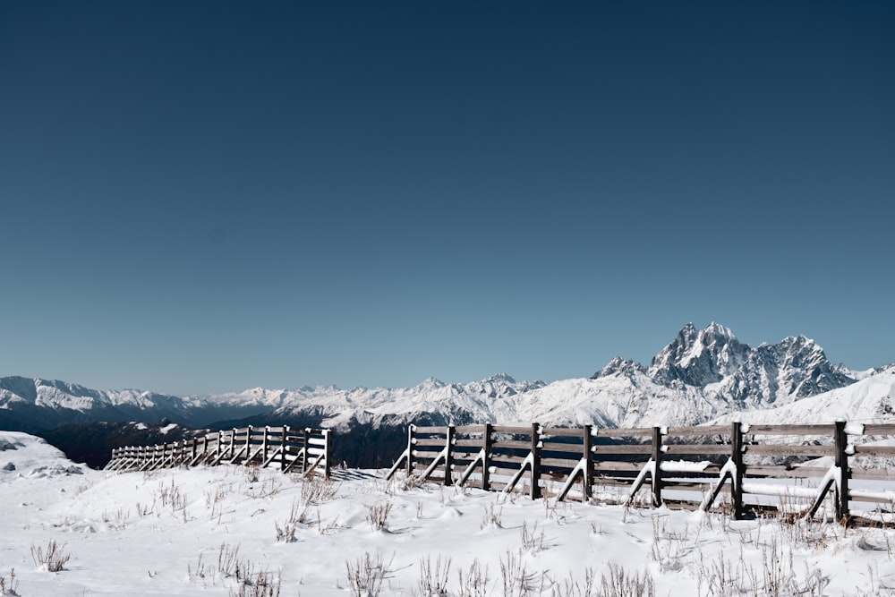 a snowy field with a fence and mountains in the background
