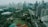 A sprawling urban landscape featuring numerous high-rise buildings with various modern architectural designs. A major roadway cuts through the cityscape, flanked by lush greenery including parks and sports fields, creating a blend of nature and urban development.