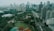 A sprawling urban landscape featuring numerous high-rise buildings with various modern architectural designs. A major roadway cuts through the cityscape, flanked by lush greenery including parks and sports fields, creating a blend of nature and urban development.