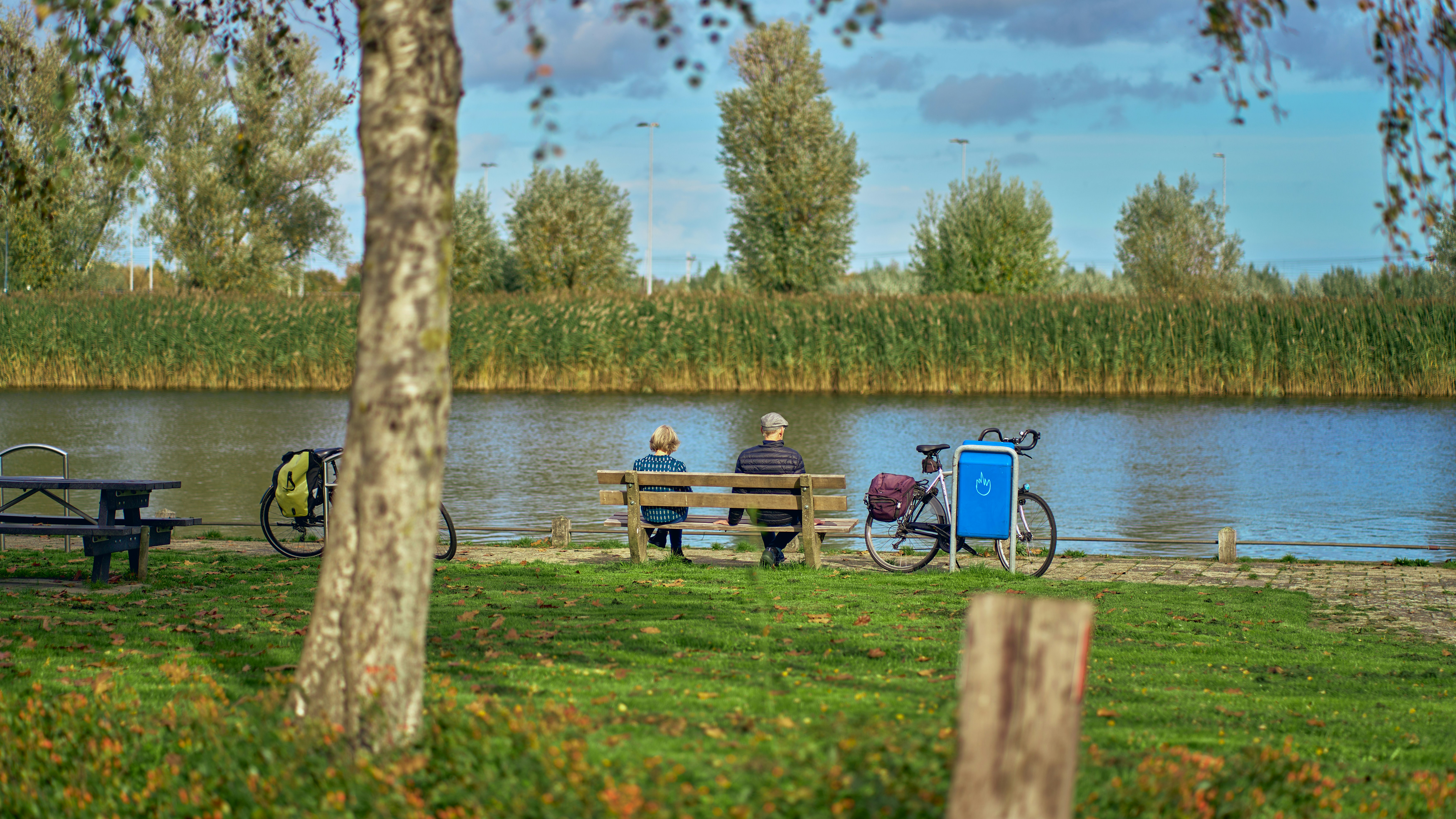 a couple of people sit on a bench by a lake