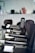 A row of black salon chairs arranged in a hair salon, with a jacket draped over one of the chairs. The background features blurred objects, possibly hair products or equipment.