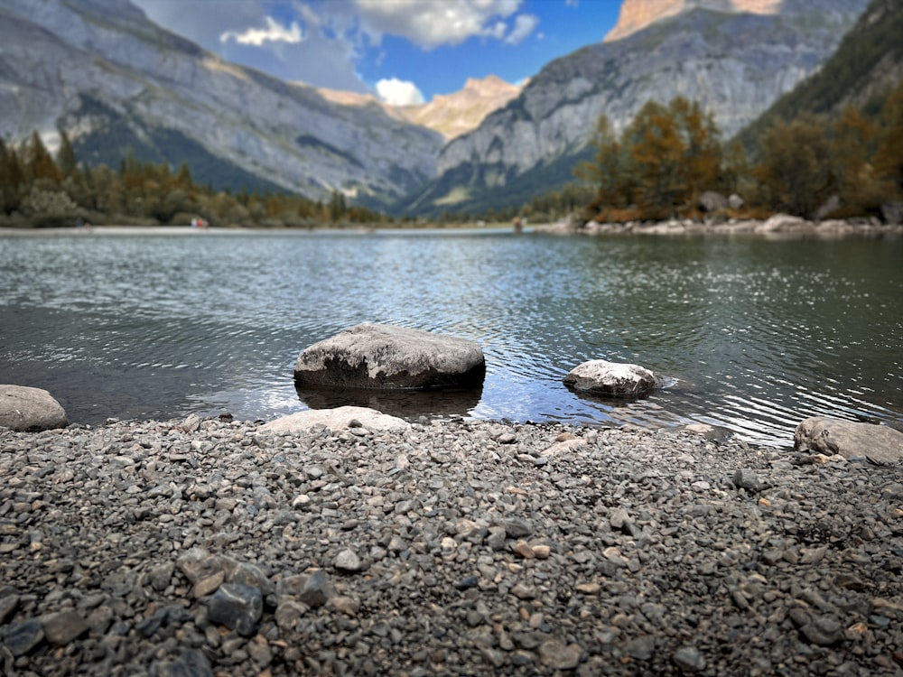 a rocky shore next to a body of water with mountains in the background