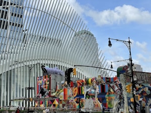 A modern architectural structure with white, rib-like extensions dominates the scene, complemented by vibrant street art and murals on nearby buildings. The sky is clear and blue, and a streetlamp with an intricate design is visible. Traffic lights and street signs indicating Church Street and Dey Street can be seen.