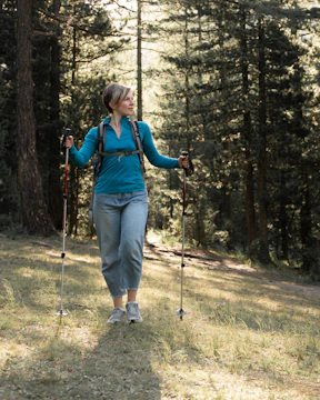 A person walking energetically through a sunlit park trail surrounded by trees.