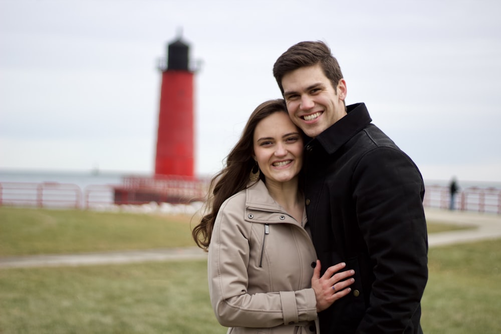 a man and woman posing for a picture in front of a lighthouse