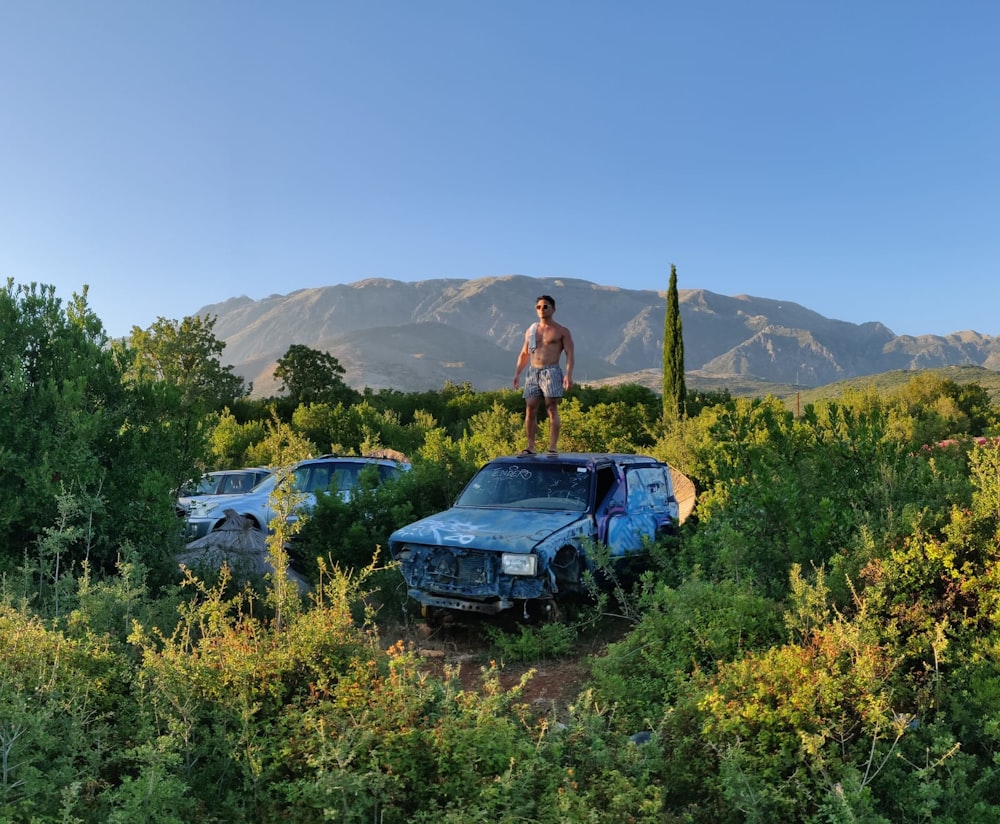 a person standing on a blue car in a field of flowers