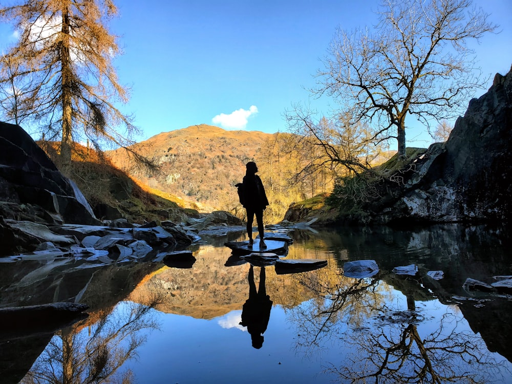 a person standing in a body of water with trees and rocks around it