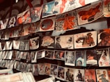 A display of vintage propaganda posters hanging on a wall, featuring various illustrations and slogans. The posters depict historical and political themes, showcasing figures in military and industrial settings, space exploration, and patriotic imagery. Many of the posters have a distinct red and black color scheme, highlighting strong and bold graphical elements.