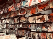 A display of vintage propaganda posters hanging on a wall, featuring various illustrations and slogans. The posters depict historical and political themes, showcasing figures in military and industrial settings, space exploration, and patriotic imagery. Many of the posters have a distinct red and black color scheme, highlighting strong and bold graphical elements.
