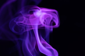 Swirling, ethereal purple smoke against a black background with soft, flowing contours and varying shades of violet.