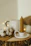 Close-up of a beige and terra cotta candle softly glowing on a rustic wooden table.