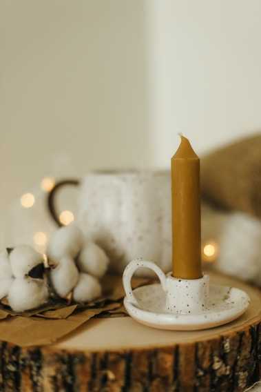 A warm, softly lit close-up of a candlestick muller resting on a textured wooden table, surrounded by scattered shells and wool fibers.
