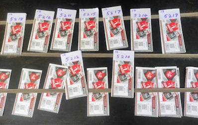 Several rows of paper tickets are arranged on a flat dark surface. Each ticket features a prominent red design with text and barcodes. The tickets are grouped in sets with handwritten labels above them, displaying numbers like '5218', '5216', and others.