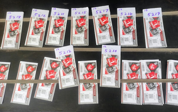 Several rows of paper tickets are arranged on a flat dark surface. Each ticket features a prominent red design with text and barcodes. The tickets are grouped in sets with handwritten labels above them, displaying numbers like '5218', '5216', and others.