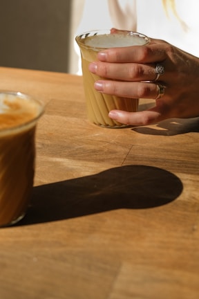 Hands adorned with delicate rings holding a coffee cup in soft natural light.