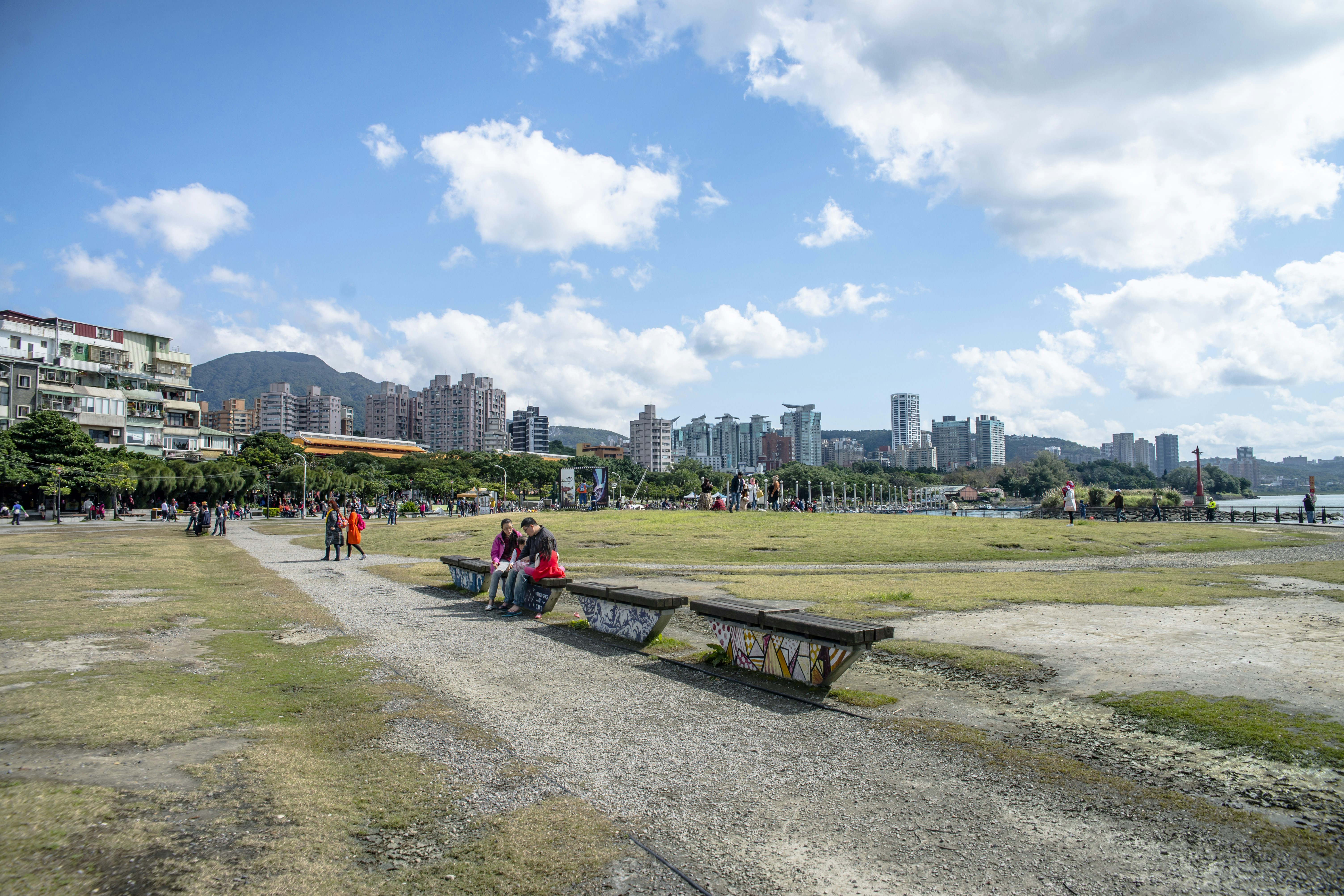 a group of people sitting on a bench in a park with a city in the background