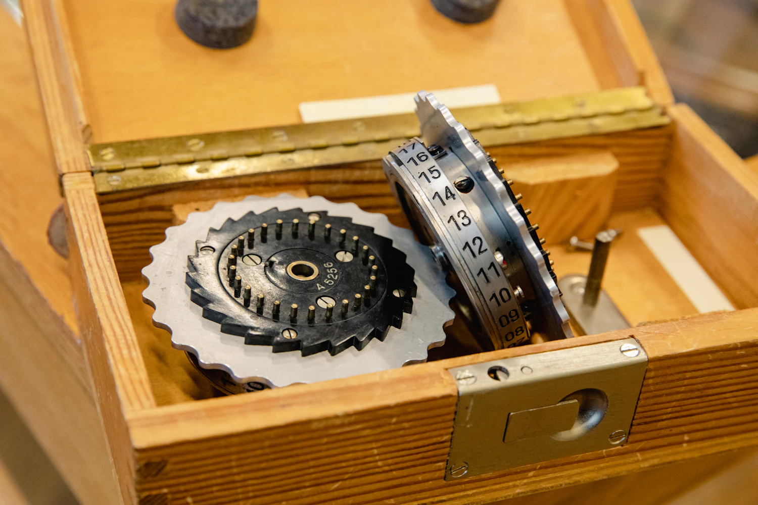 An opened wooden case on the bench showing a pinned disc and toothed wheels