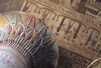 Intricate ancient Egyptian hieroglyphics and artwork adorn the ceiling and columns, featuring colorful depictions of figures and symbols.
