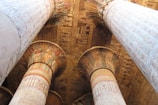 Large, intricately carved columns adorned with detailed hieroglyphics and colorful painted patterns. The ceiling is rich with Egyptian motifs and symbols, showcasing ancient artistic craftsmanship.
