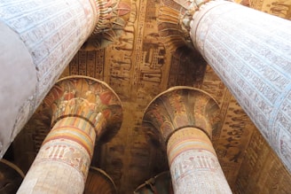 Large, intricately carved columns adorned with detailed hieroglyphics and colorful painted patterns. The ceiling is rich with Egyptian motifs and symbols, showcasing ancient artistic craftsmanship.