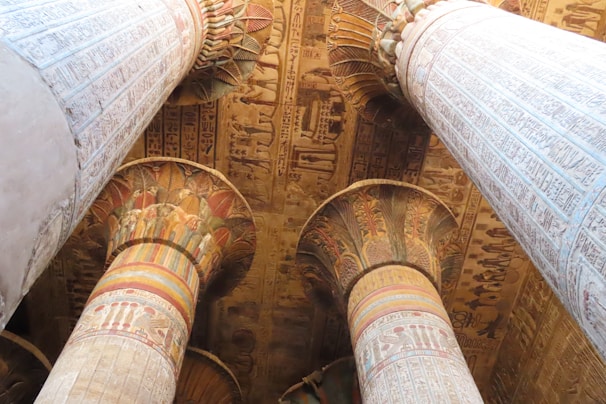 Large, intricately carved columns adorned with detailed hieroglyphics and colorful painted patterns. The ceiling is rich with Egyptian motifs and symbols, showcasing ancient artistic craftsmanship.