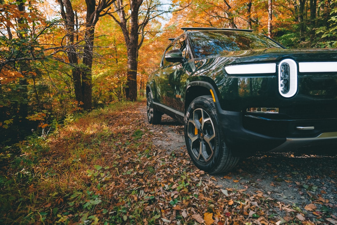 Forest Green Rivian R1T electric truck driving on a gravel road in the blue ridge mountains during fall