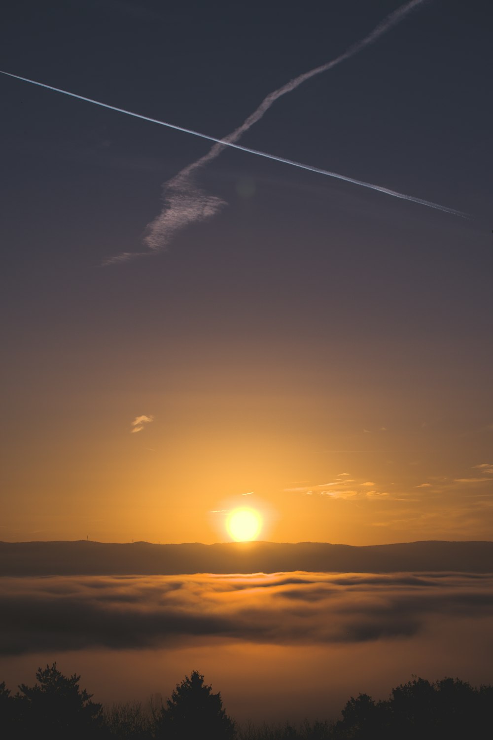 a sunset with clouds and a jet trail