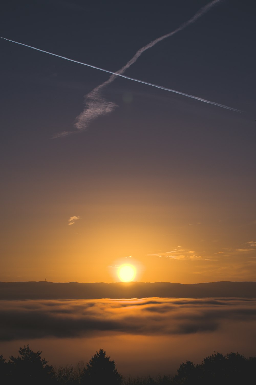 Un coucher de soleil avec des nuages et une traînée de jet