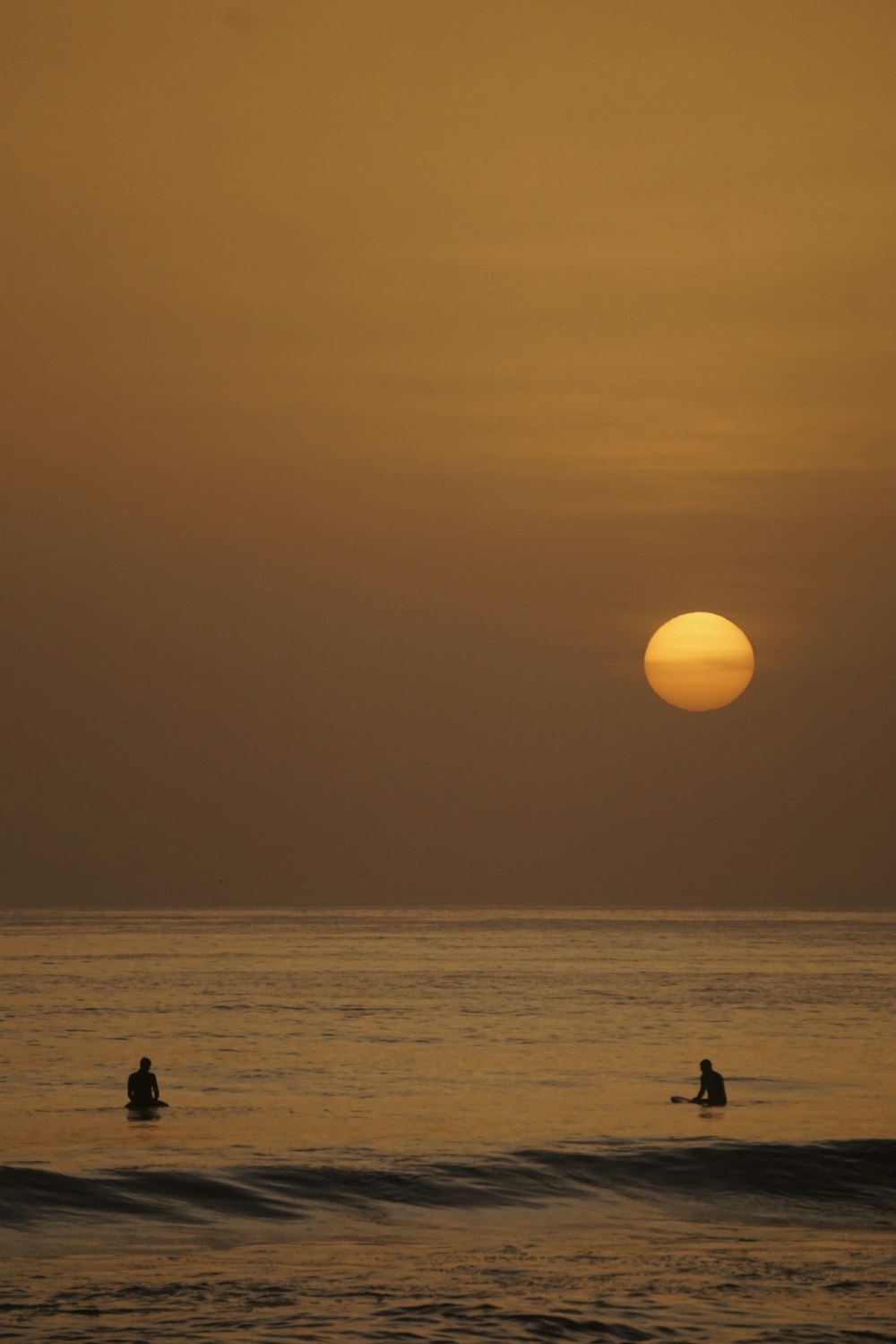 a couple people in the water with the sun in the background