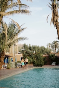 a couple of people standing by a pool with palm trees and a building