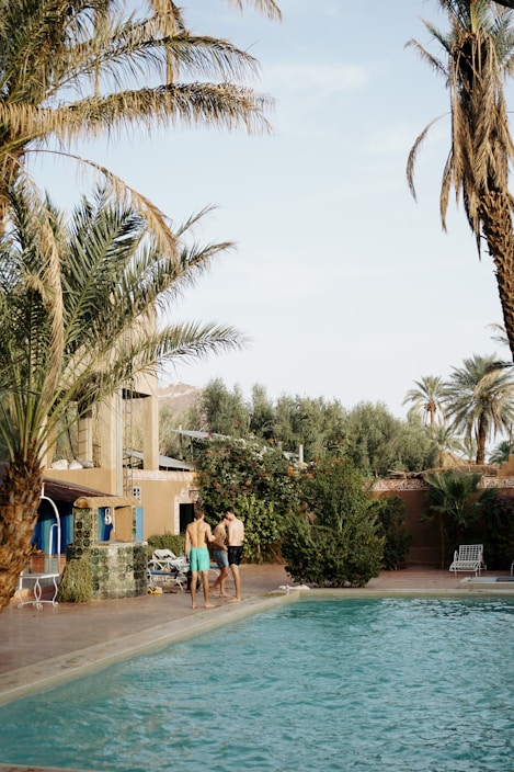 a couple of people standing by a pool with palm trees and a building