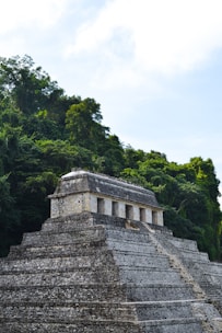 An ancient stone pyramid structure surrounded by dense green jungle vegetation, showcasing a blend of man-made architecture and natural beauty under a bright blue sky.